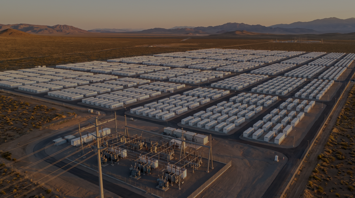 Utility-scale Battery Energy Storage System (BESS) installation at sunset — large grid of lithium-ion battery enclosures with power substation and mountains in the background